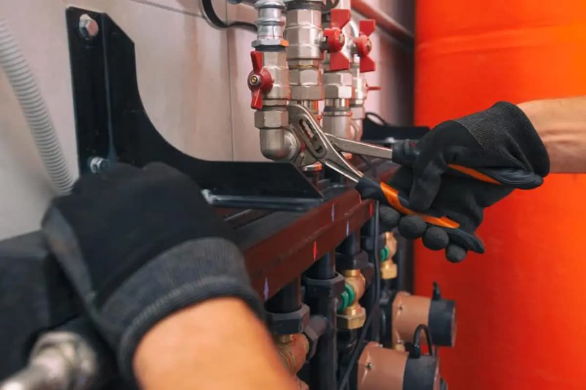 Gloved plumber repairing pipework with tools