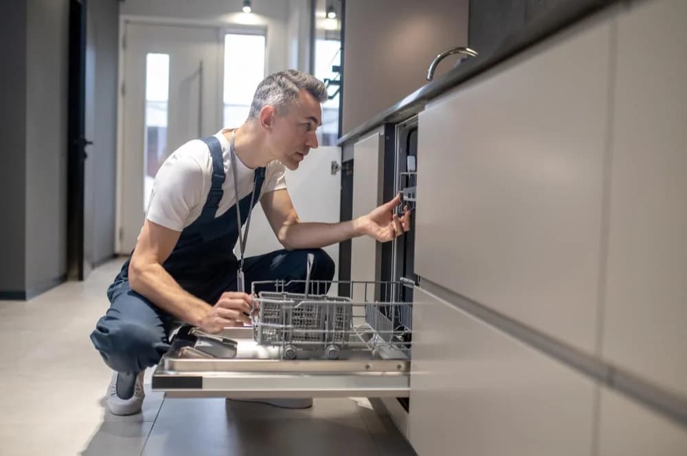 Plumber inspecting an open integrated dishwasher in a kitchen