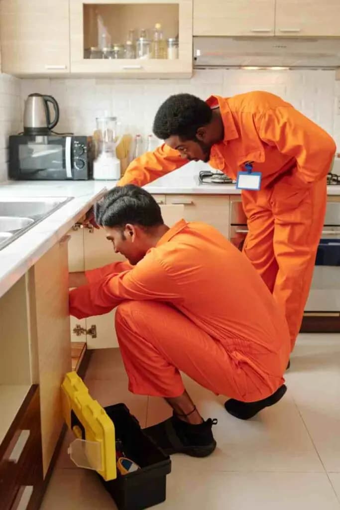 Plumbers checking pipework beneath a kitchen sink during an emergency enquiry in Surbiton